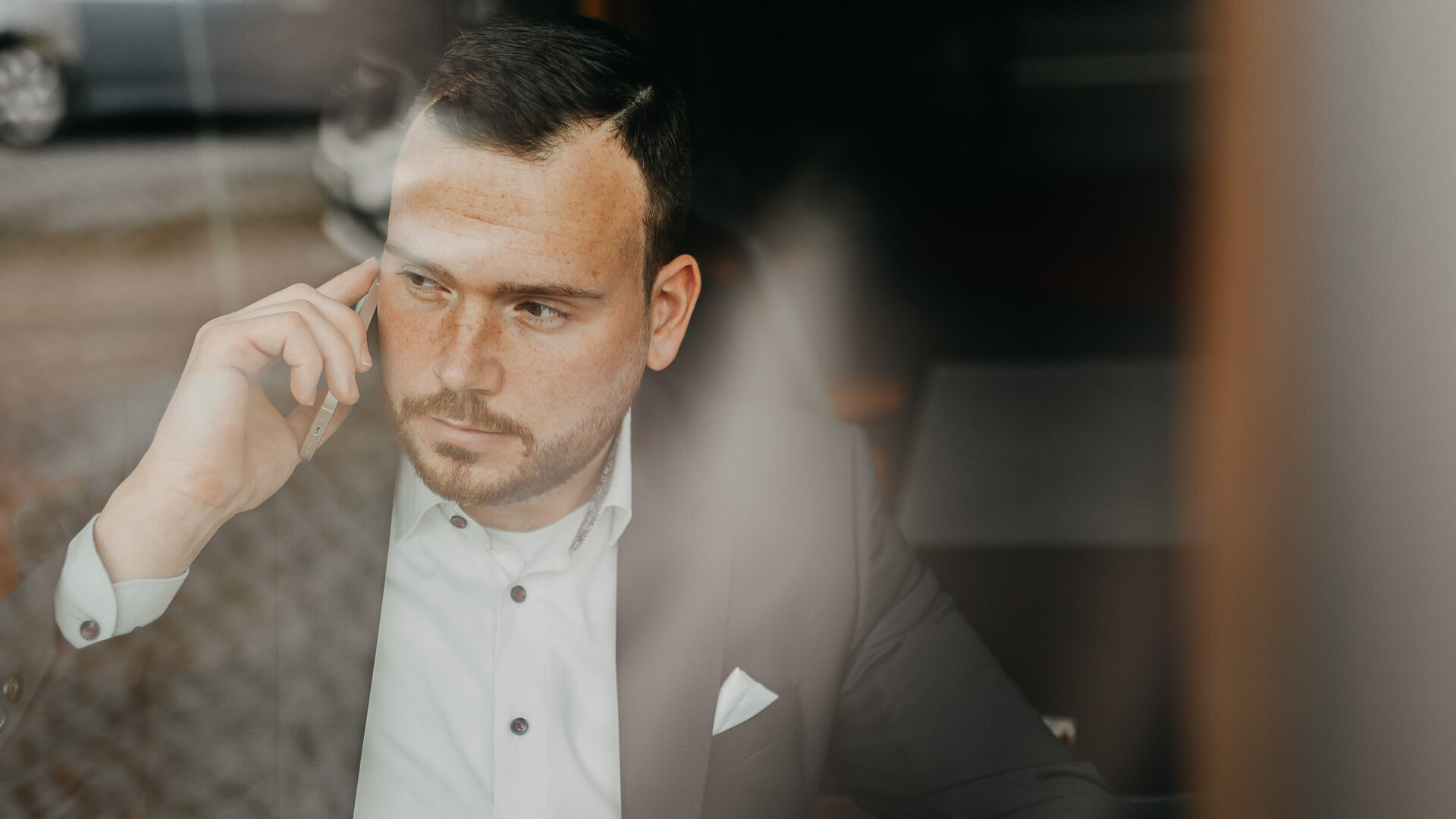 Ein Symbolbild: Ein telefonierender Mann im Anzug durch eine Glasscheibe fotografiert.